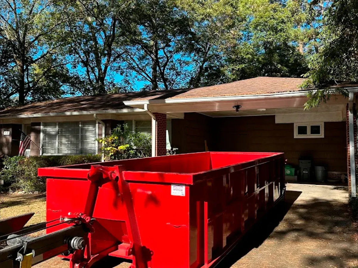 A red dumpster is parked in front of a house.