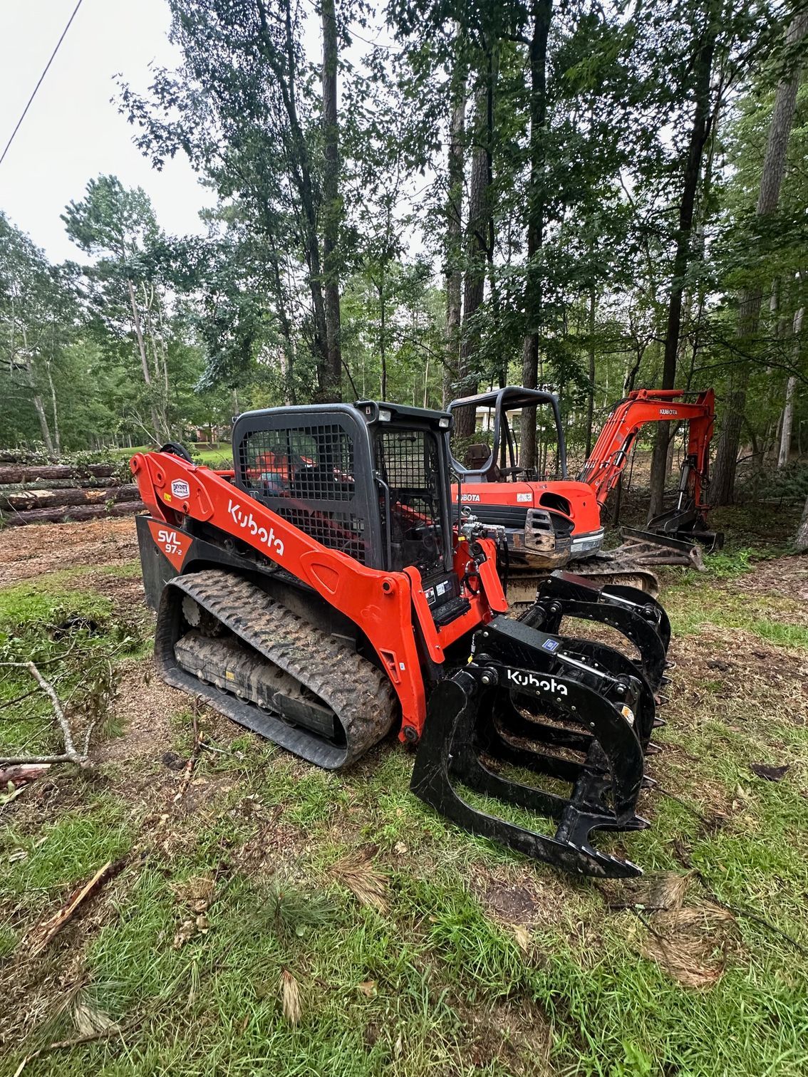 A bulldozer with a grapple attached to it is parked in a grassy field.
