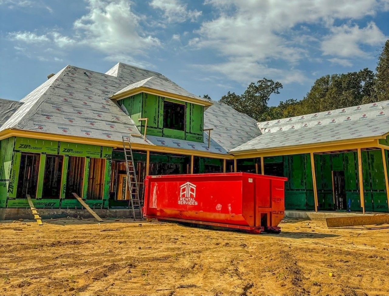 A large house under construction with a red dumpster in front of it.