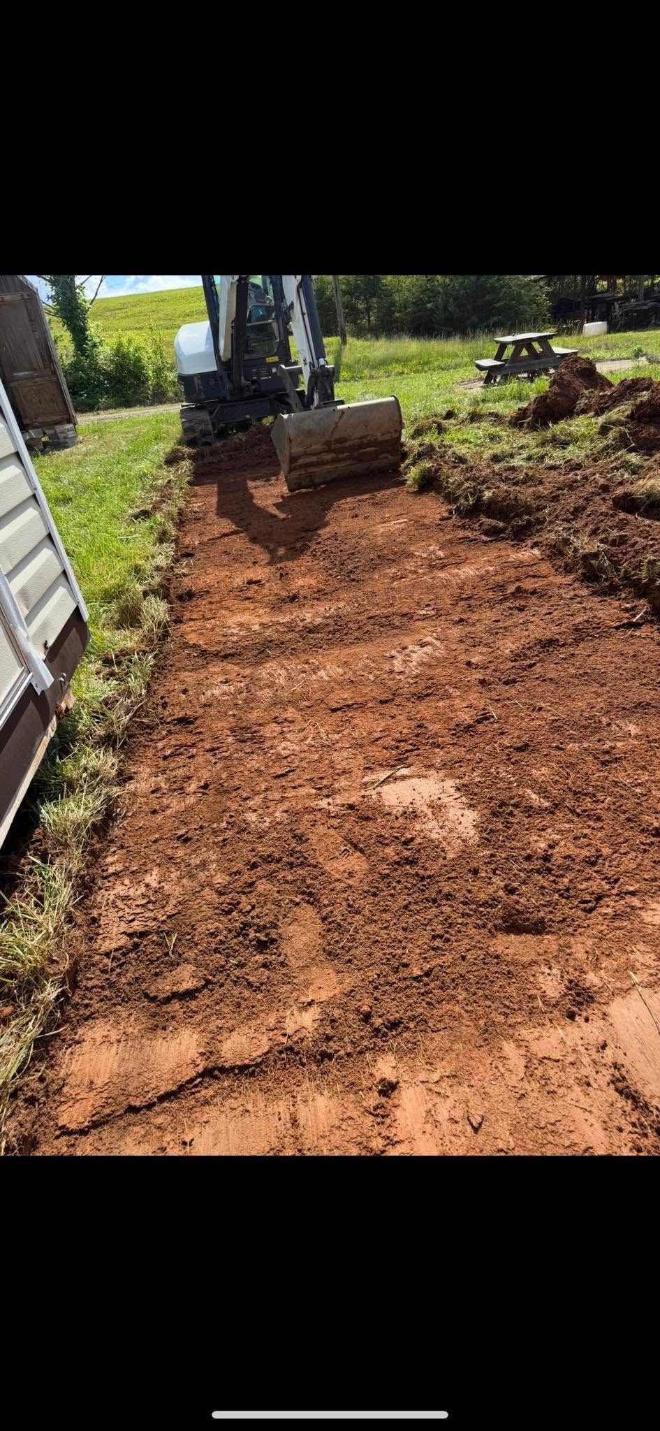 Freshly cleared dirt path beside a white building, leading to a stacked stone step in a sunny yard