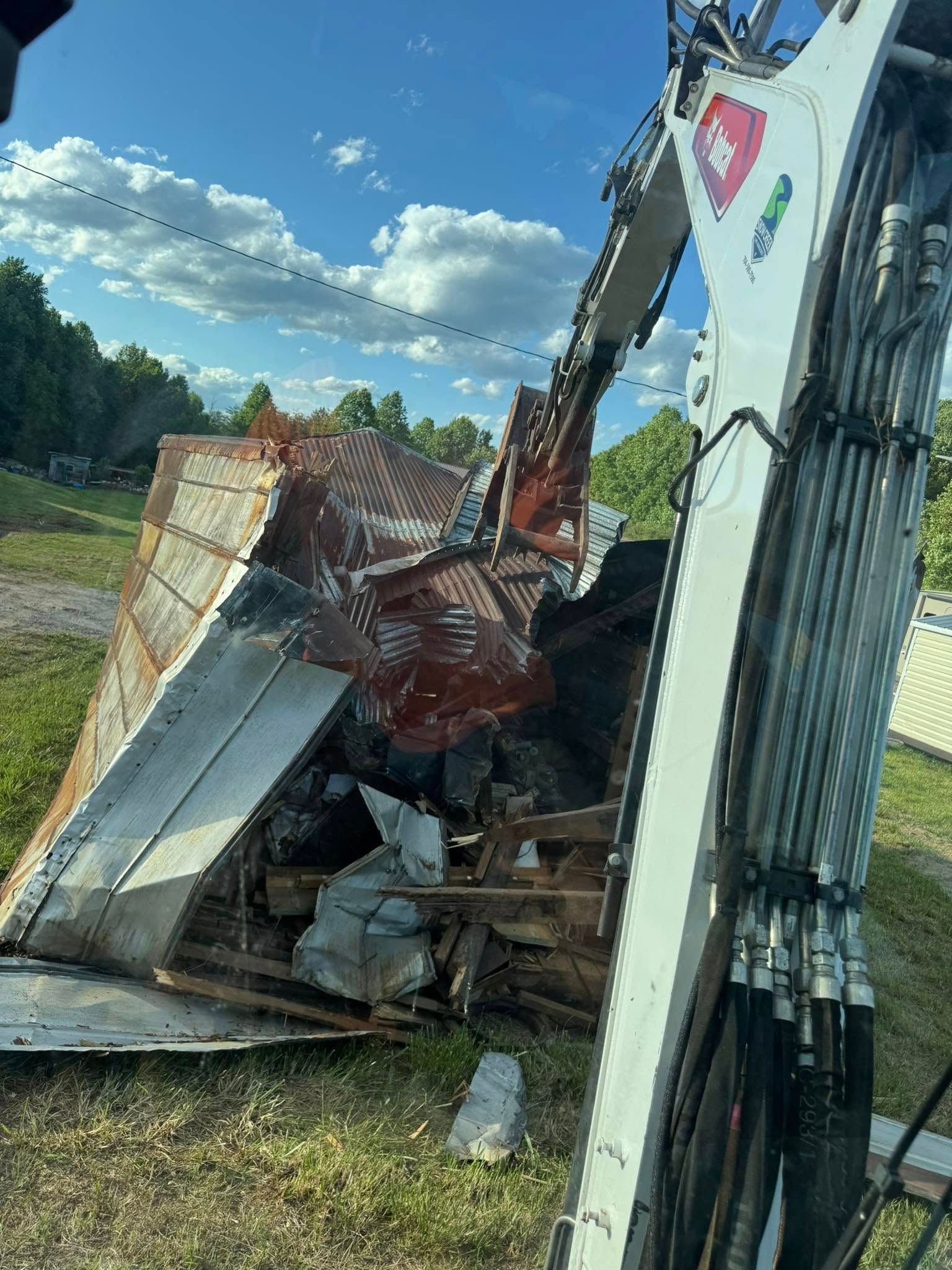 Severe roadside accident with overturned truck, crushed trailer, and debris in a grassy field under a blue sky