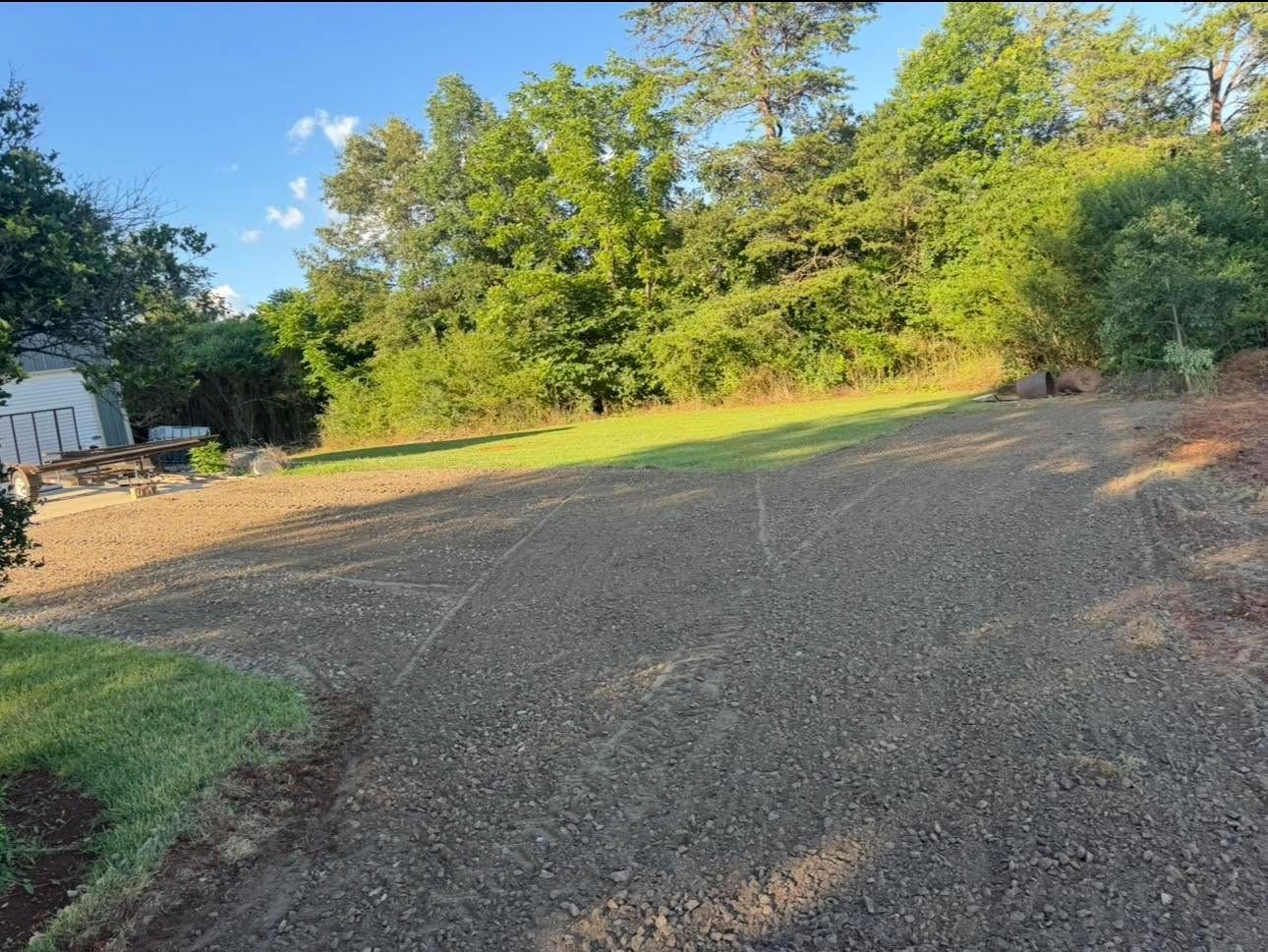 Gravel driveway beside trees and grass under a clear blue sky