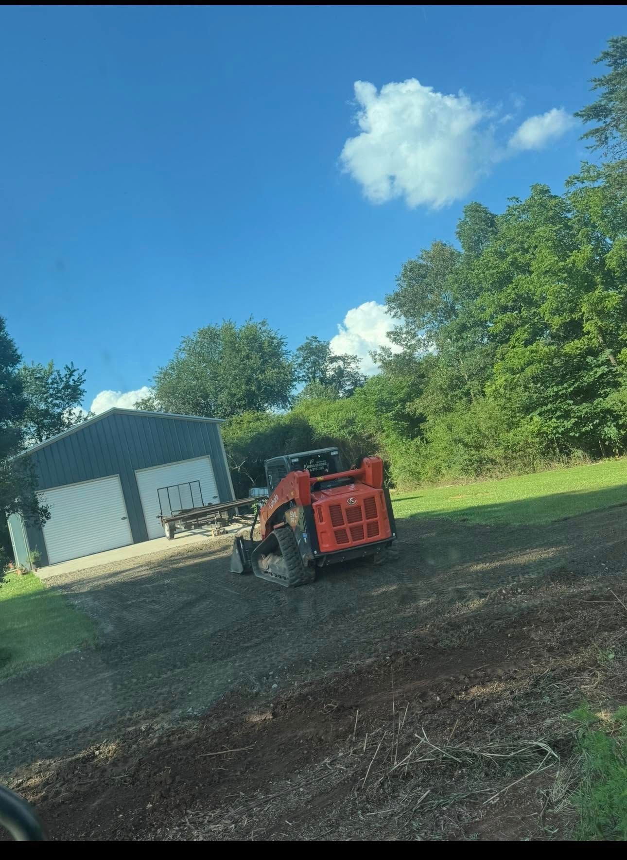 Red forklift on gravel near a white building under a blue sky with trees.
