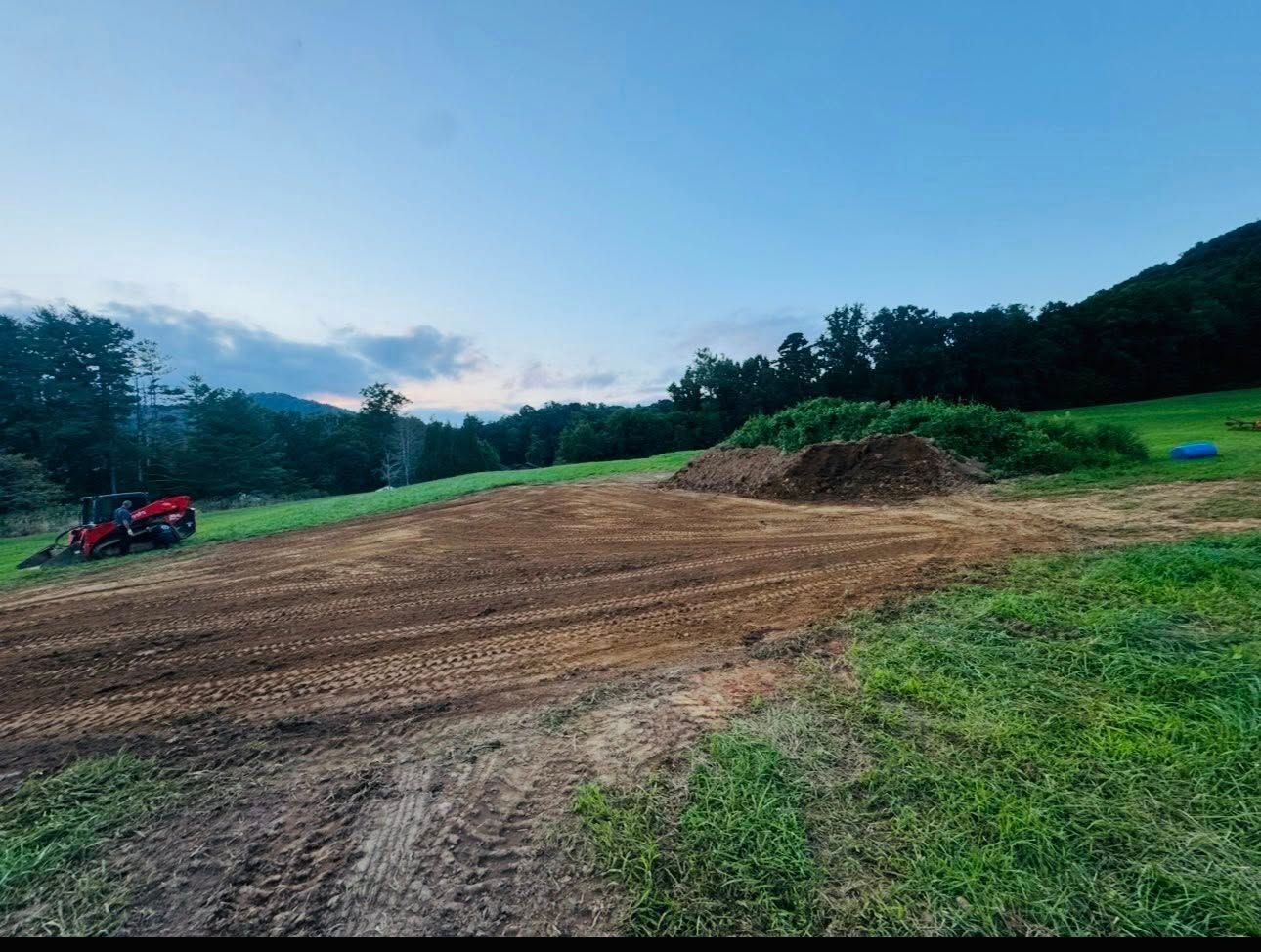 Dirt track at dusk with a red ATV on the left and a small dirt mound in a grassy field.