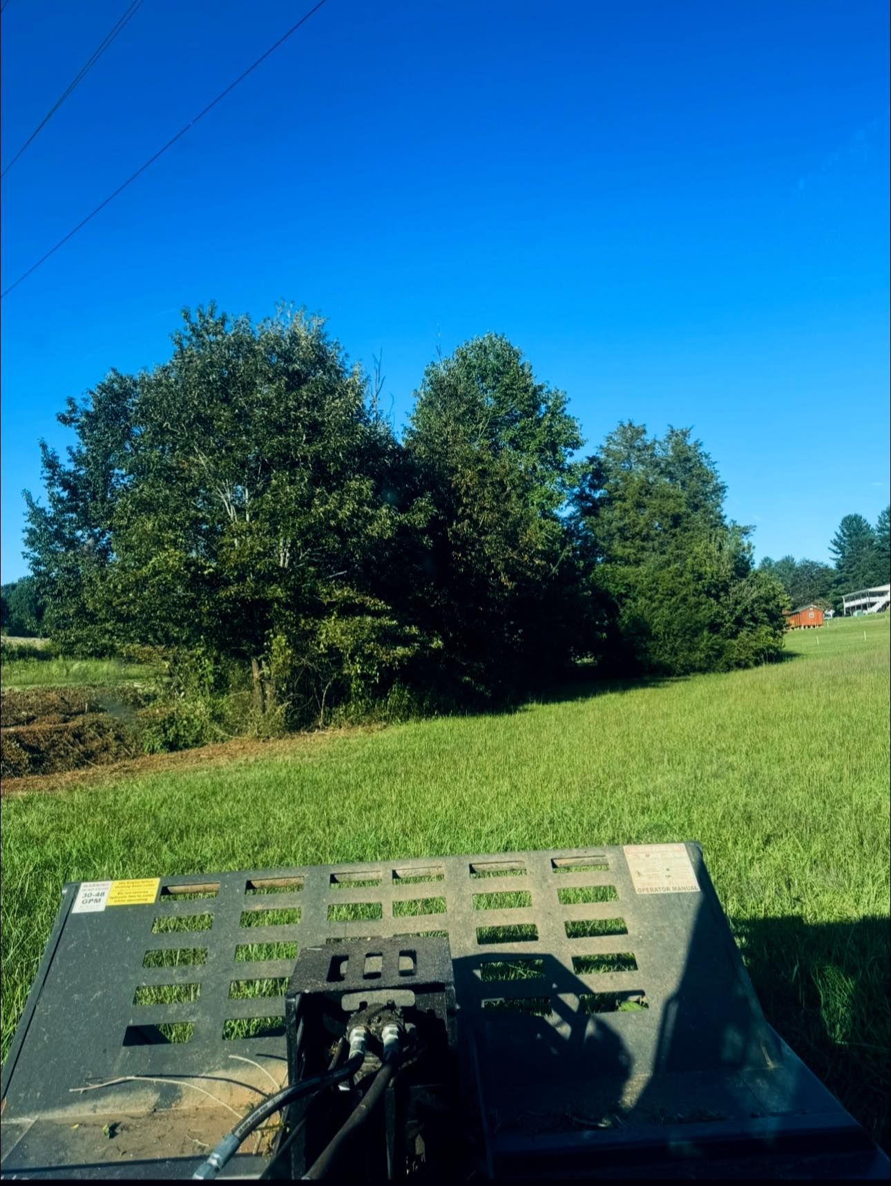 Farm view from a tractor, with green field, trees, and blue sky.