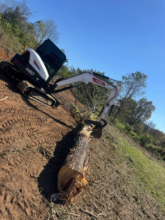 Excavator clearing a dirt trench in a grassy field under a clear blue sky