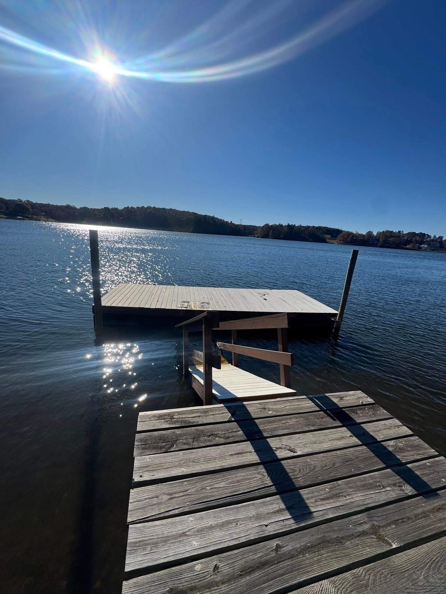Wooden dock extending into a sparkling lake under a bright blue sky