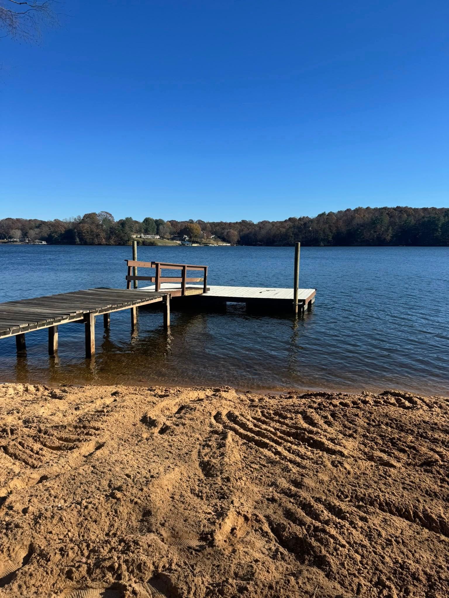 Sandy beach with a wooden dock extending into a calm blue lake under a clear sky