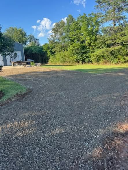 Gravel driveway beside a white building and green trees under a bright blue sky