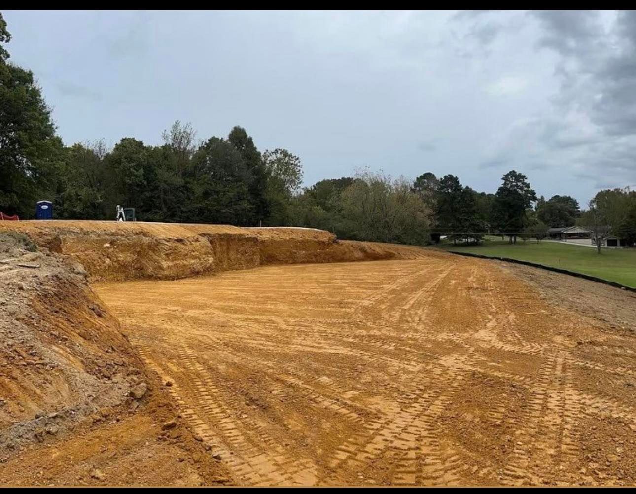 Freshly cleared dirt field beside a tree line under a cloudy sky