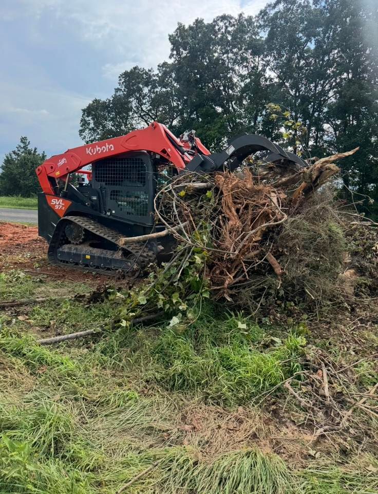 Red tracked loader pushing a pile of roots and brush in a muddy field under cloudy sky