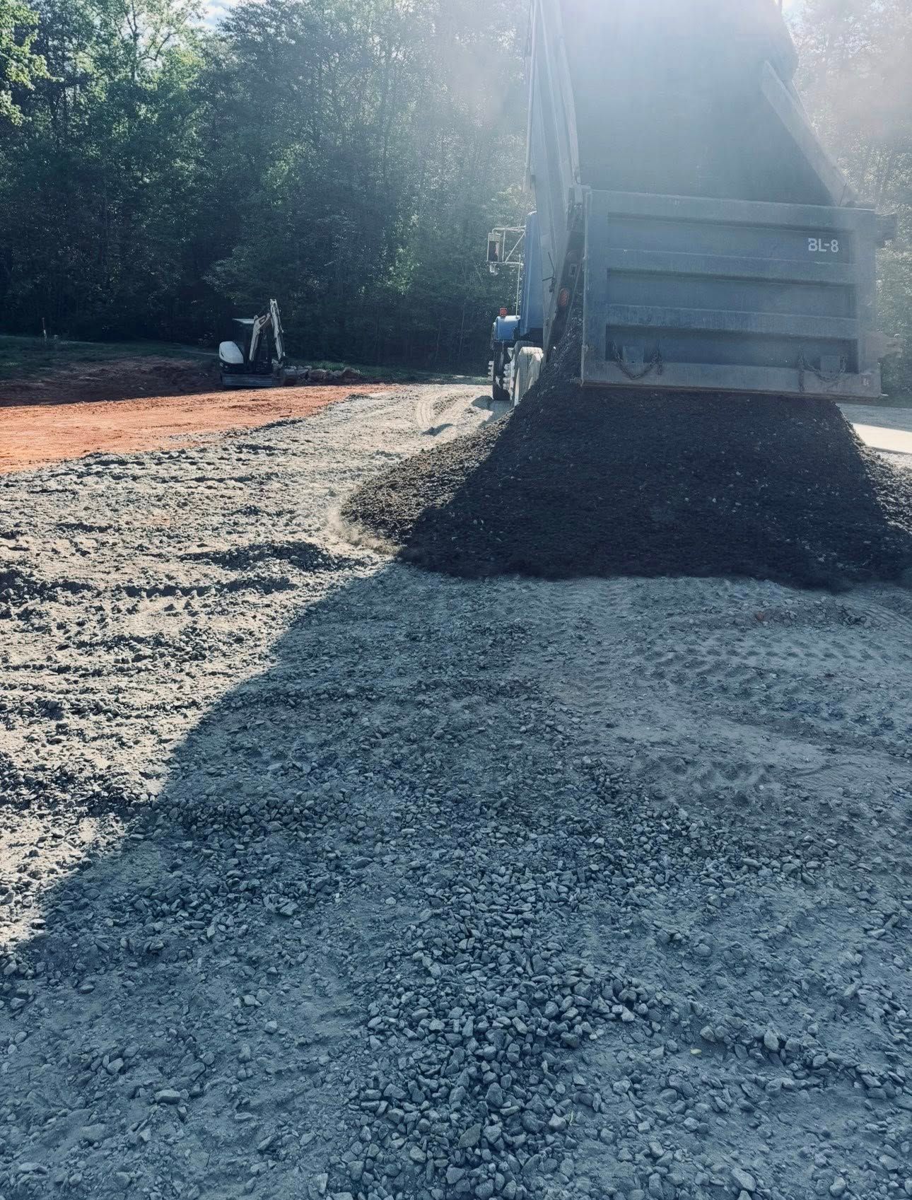 Dump truck unloading gravel onto a dirt and gravel road in a wooded area