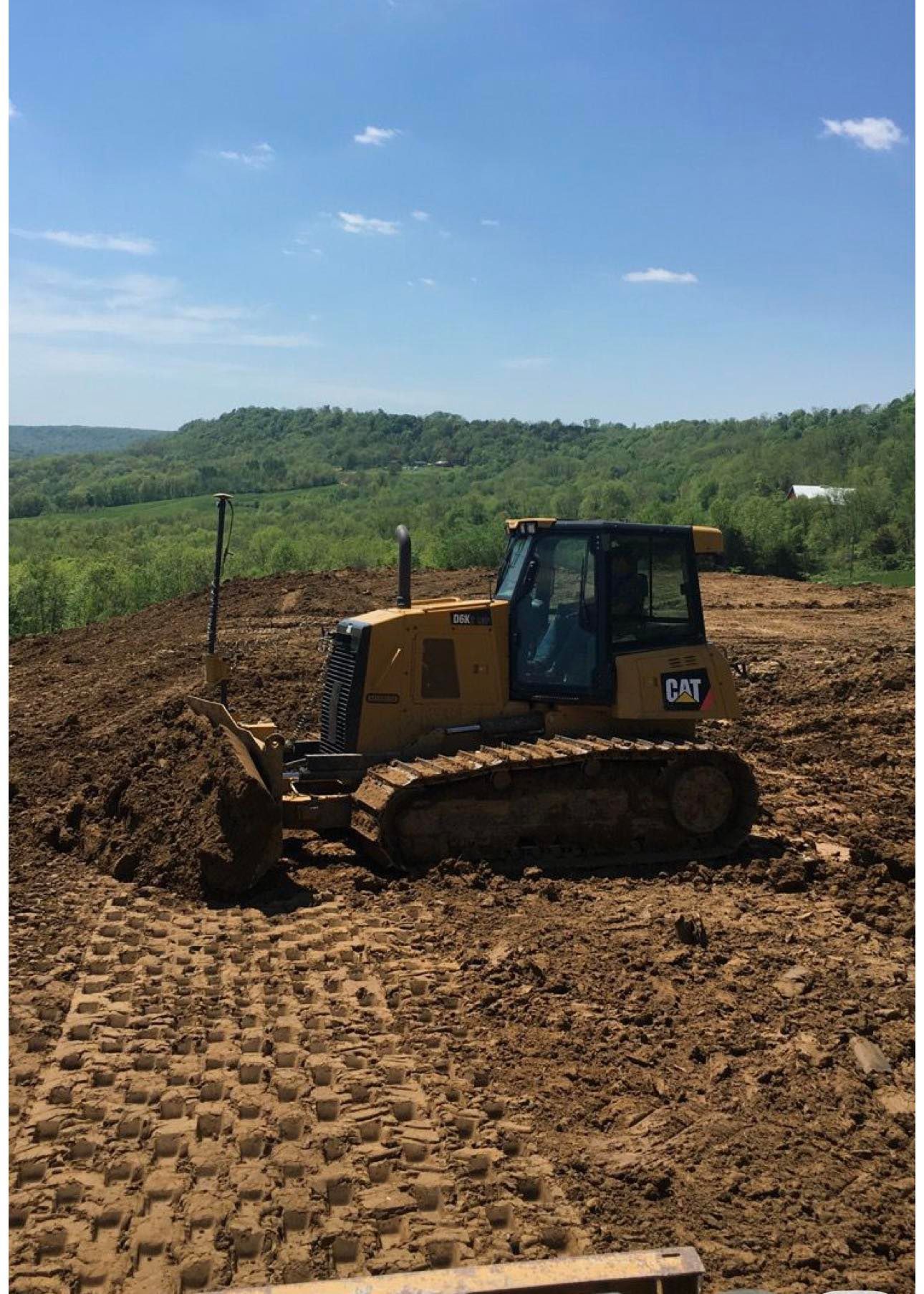 Yellow bulldozer clearing dirt on a hillside construction site under a blue sky