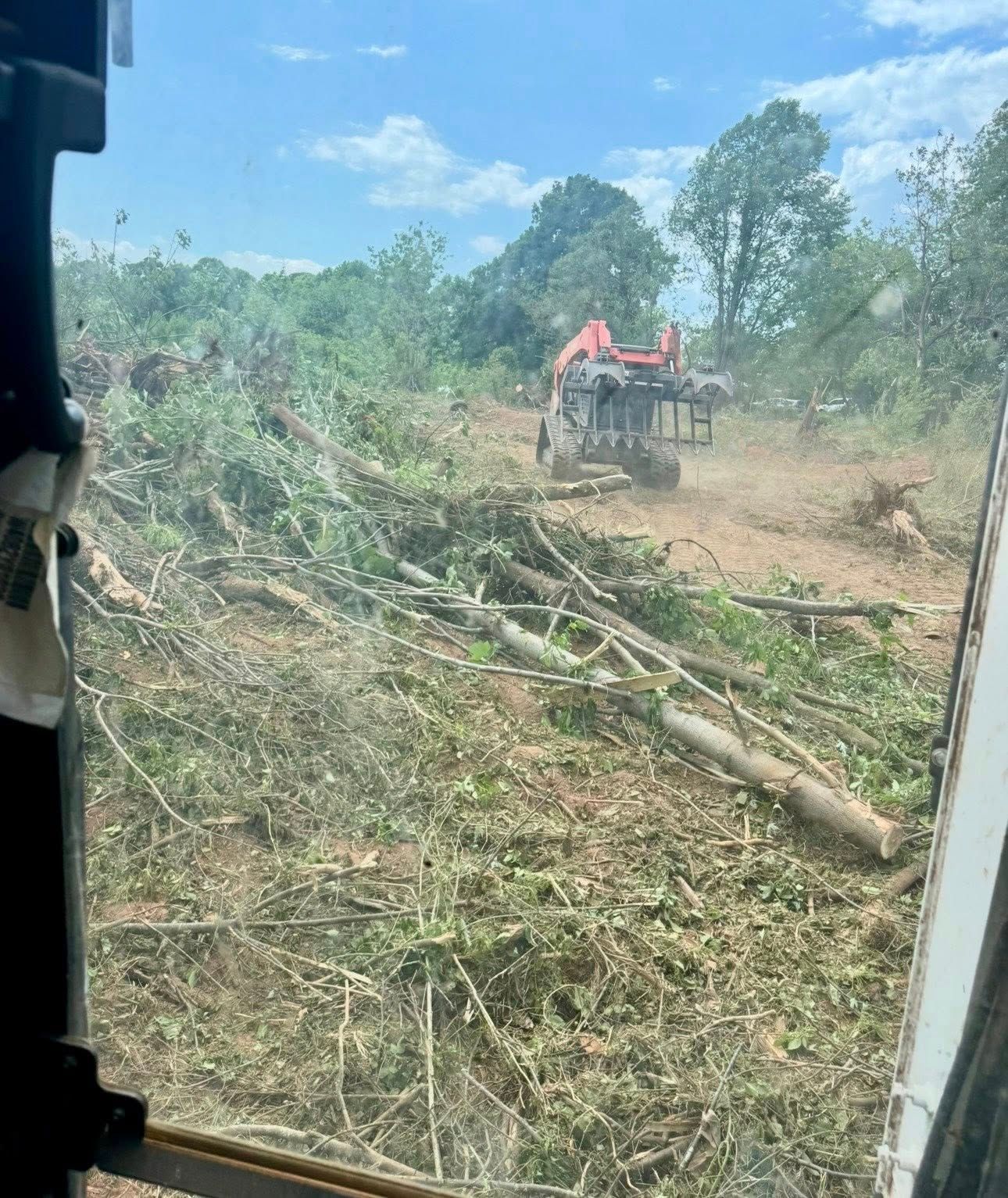 A tractor clears brush on a dusty hillside under a blue sky.