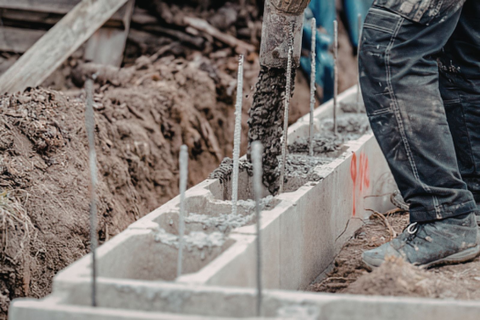Worker pouring concrete into cinder block foundation trench on a construction site