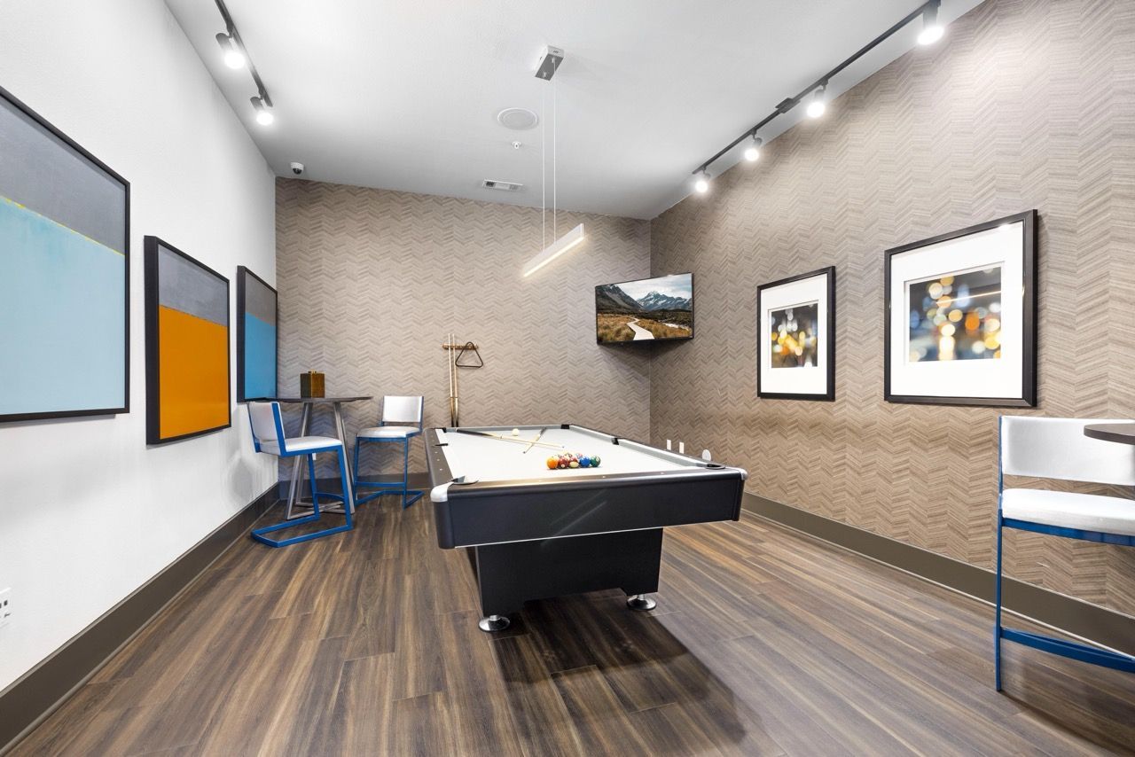 Indoor community recreation room with a pool table, wall art, and seating at Olympus at Waterside Estates, offering luxury apartments in Richmond, TX.