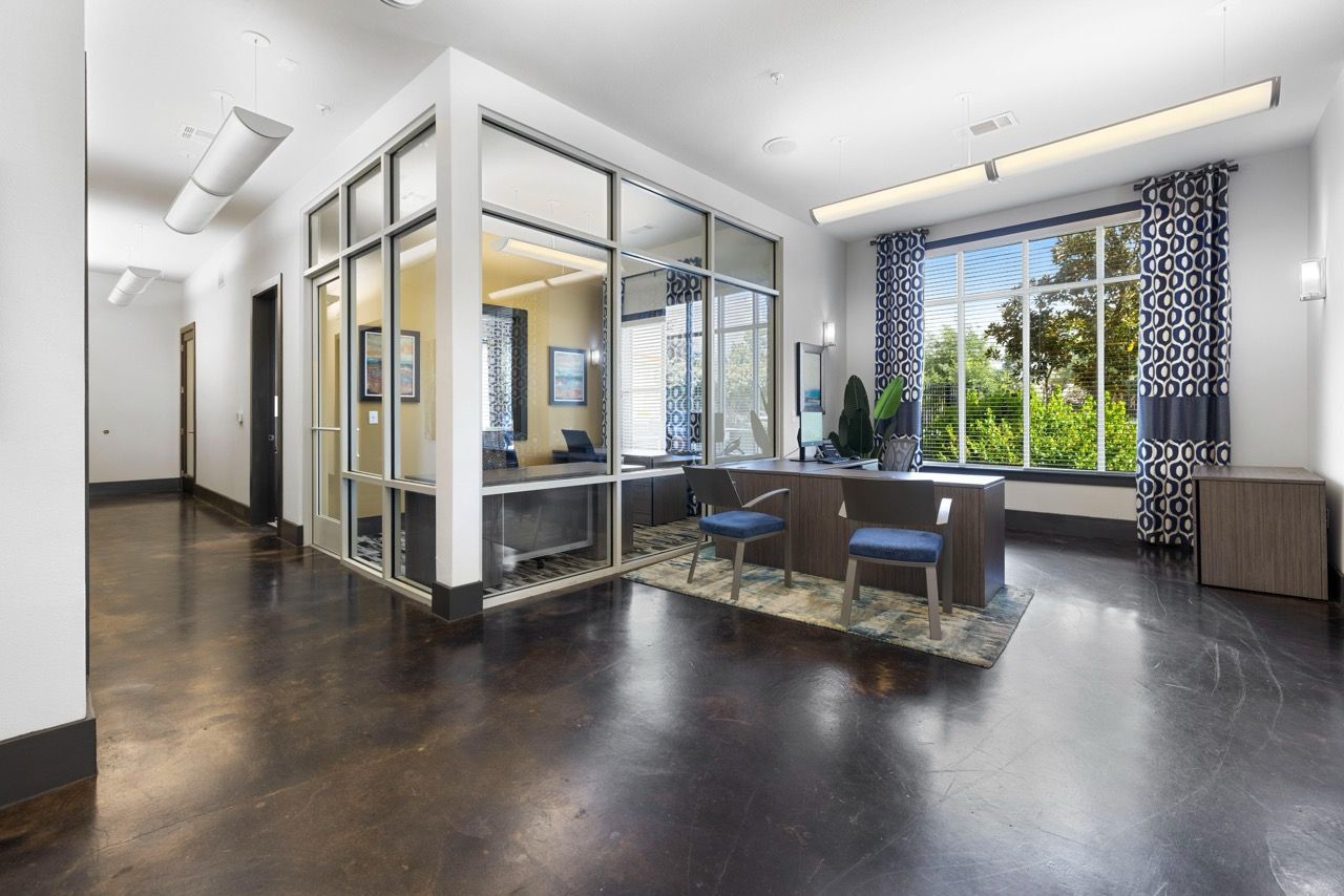 Lobby-style leasing office with glass partitions, a reception desk, and blue chairs at Olympus at Waterside Estates, offering luxury apartments for rent in Richmond, TX.
