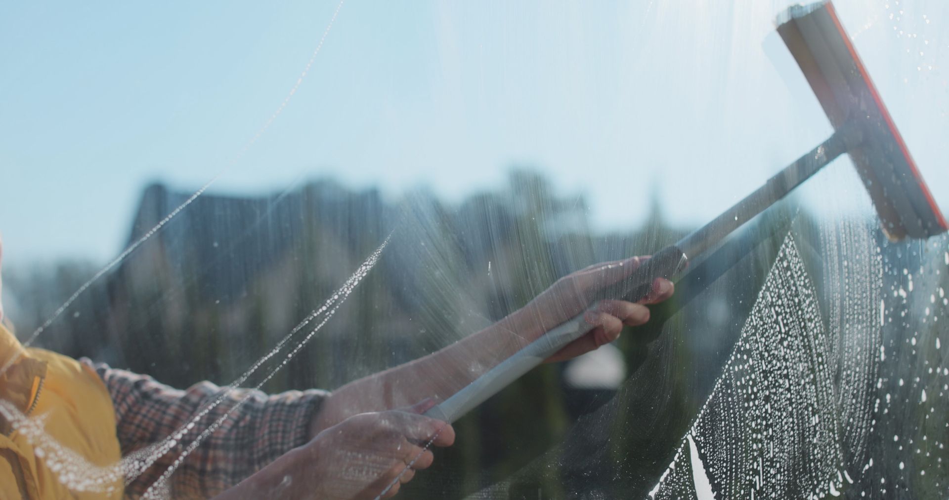 Person using a squeegee to clean a window, streaks of water and bubbles visible.