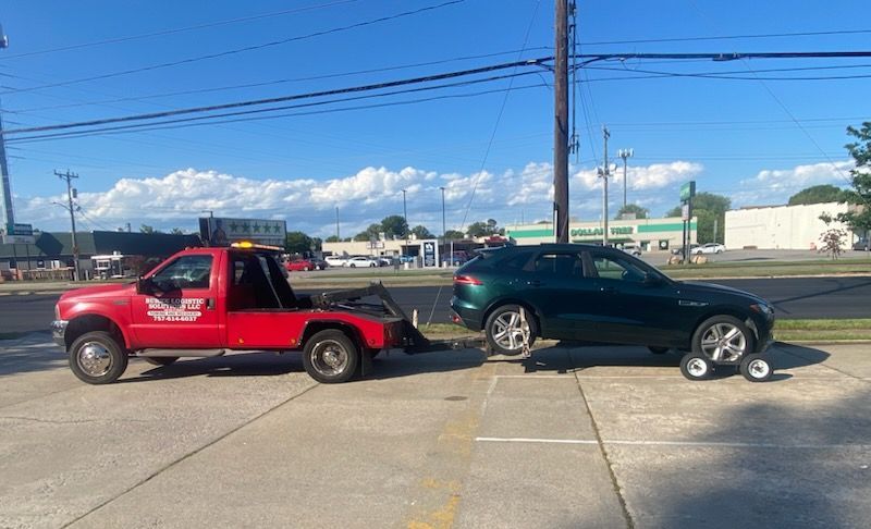 Red tow truck towing a green SUV on a sunny day. Car is on dollies.