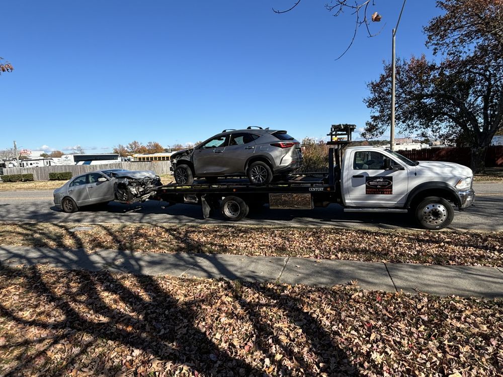 Tow truck carrying two damaged vehicles on a sunny street.