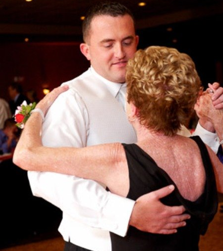A person in a white dress shirt and vest dancing with a partner wearing a black dress in a dimly lit indoor setting.