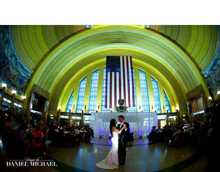Woman and man in formal attire dancing at a wedding reception; chandelier in background.