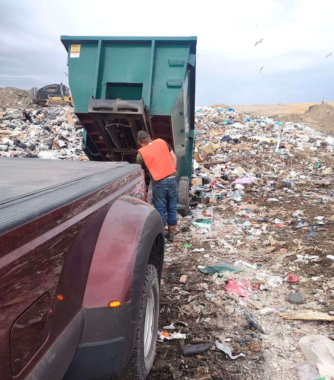 A man in an orange vest is standing in front of a dumpster