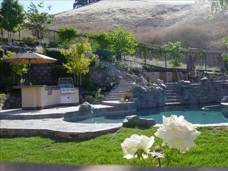 Backyard pool with stone steps, patio umbrellas, and white flowers in the foreground