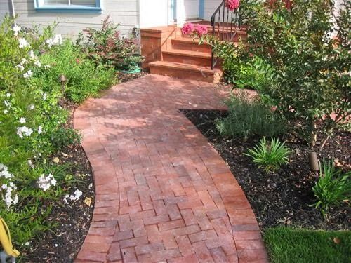 A sidewalk beside a paved road and a concrete block wall, featuring a strip of red pavers next to gray square tiles.