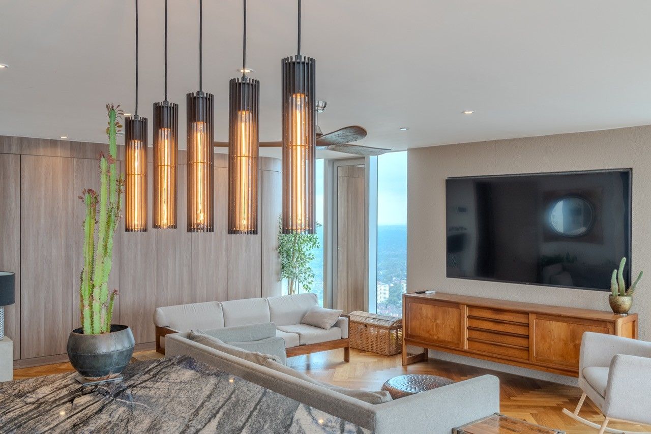 Modern living room with hanging lights, sofa, TV, and wooden cabinet, ocean view.