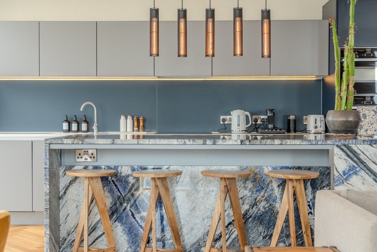 Modern kitchen with blue marble island, wooden stools, and pendant lights.