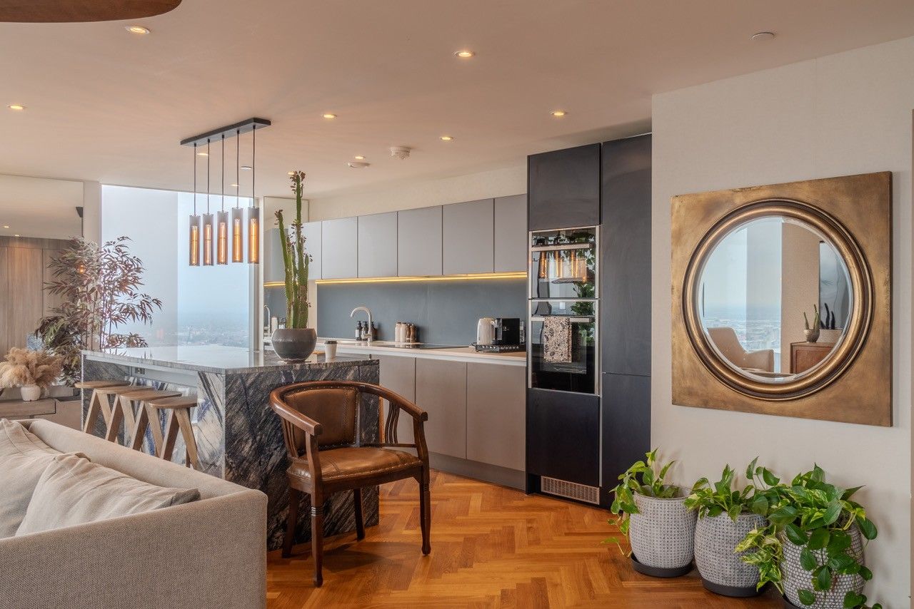 Modern kitchen with marble island, grey cabinetry, wood floor, chair, and large circular mirror.