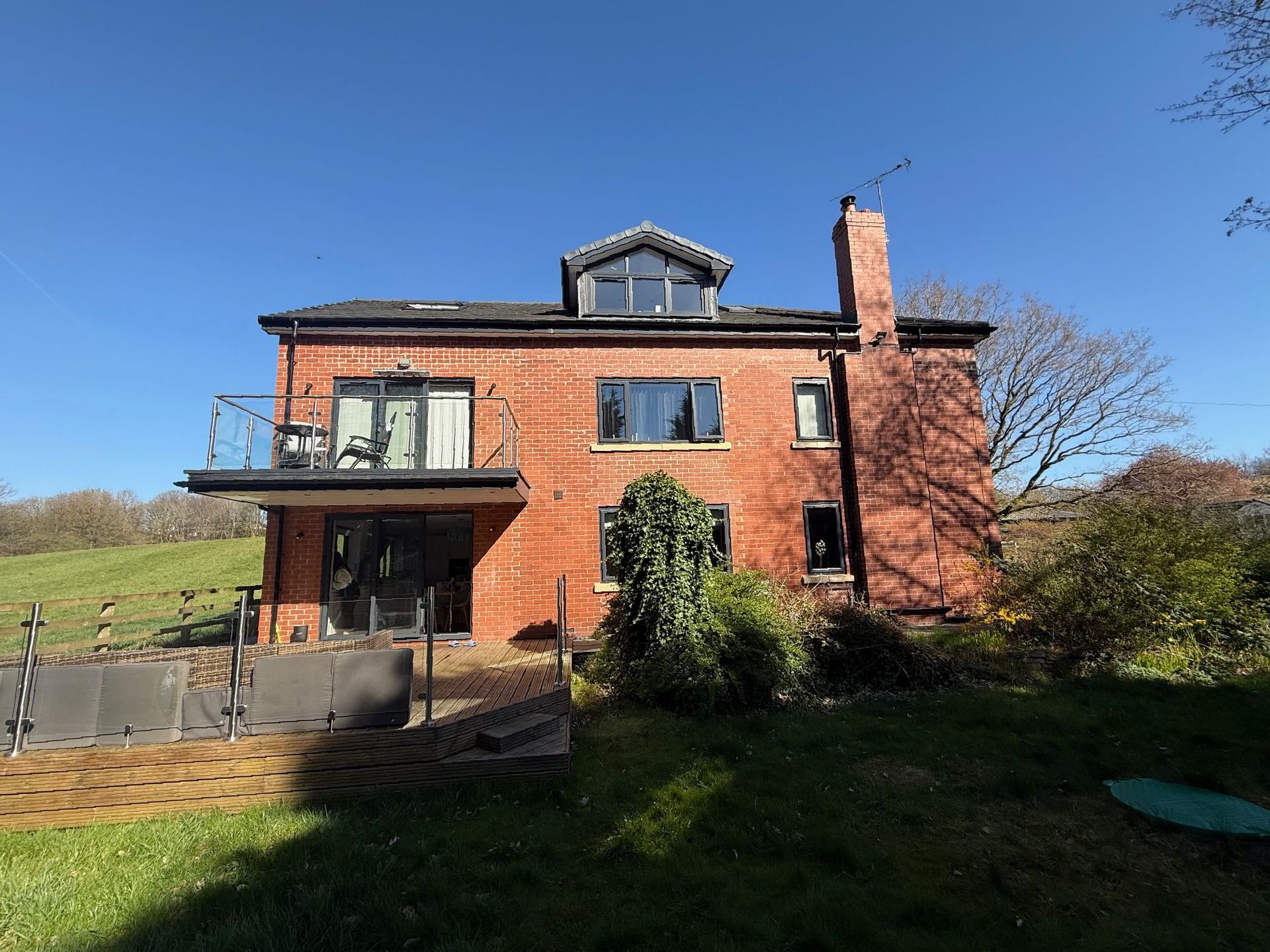 Red brick house with glass balcony, chimney, and dormer window on a sunny day.