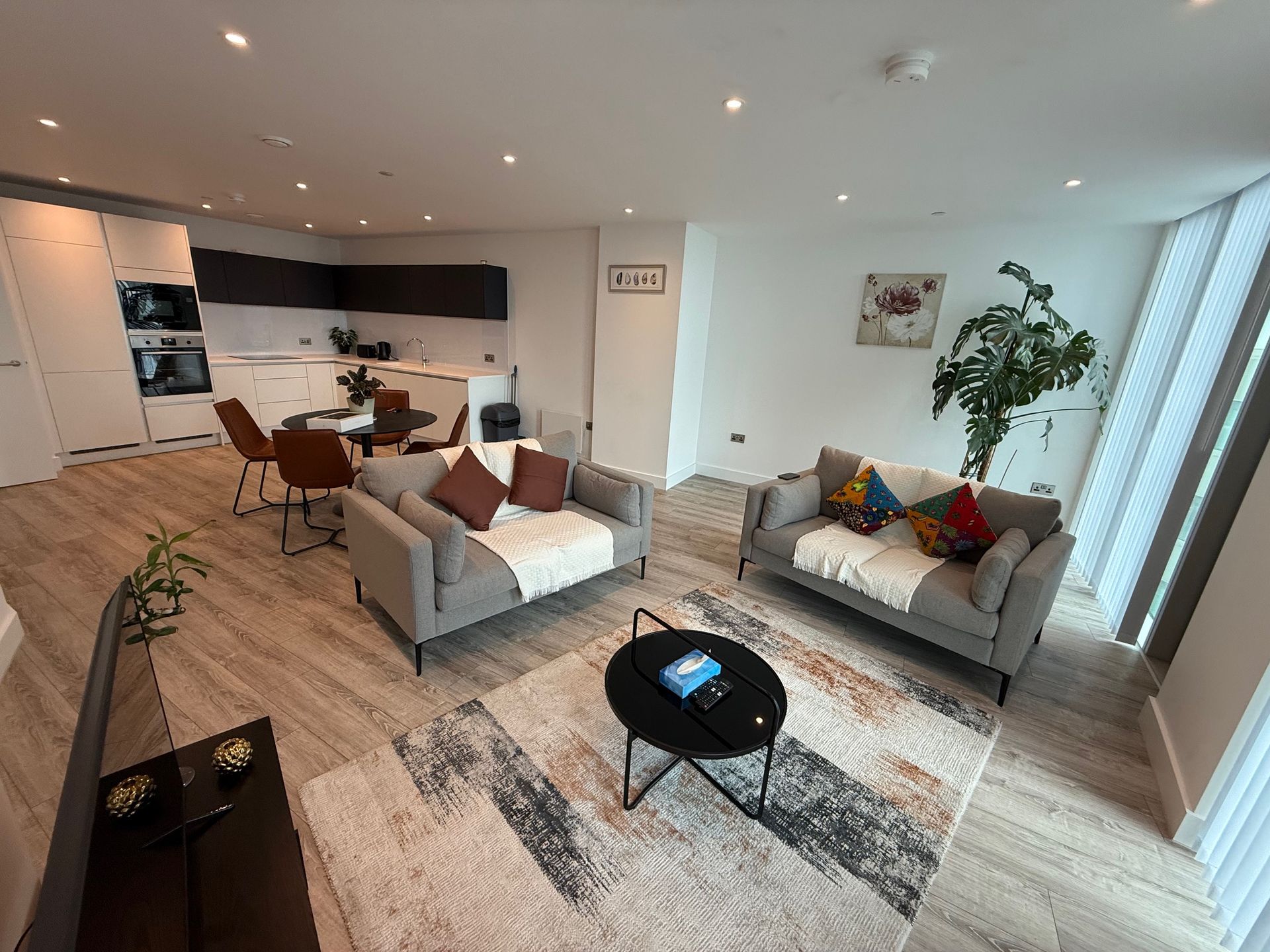Modern open-plan living space: gray sofas, black coffee table, kitchen, dining area, hardwood floors.