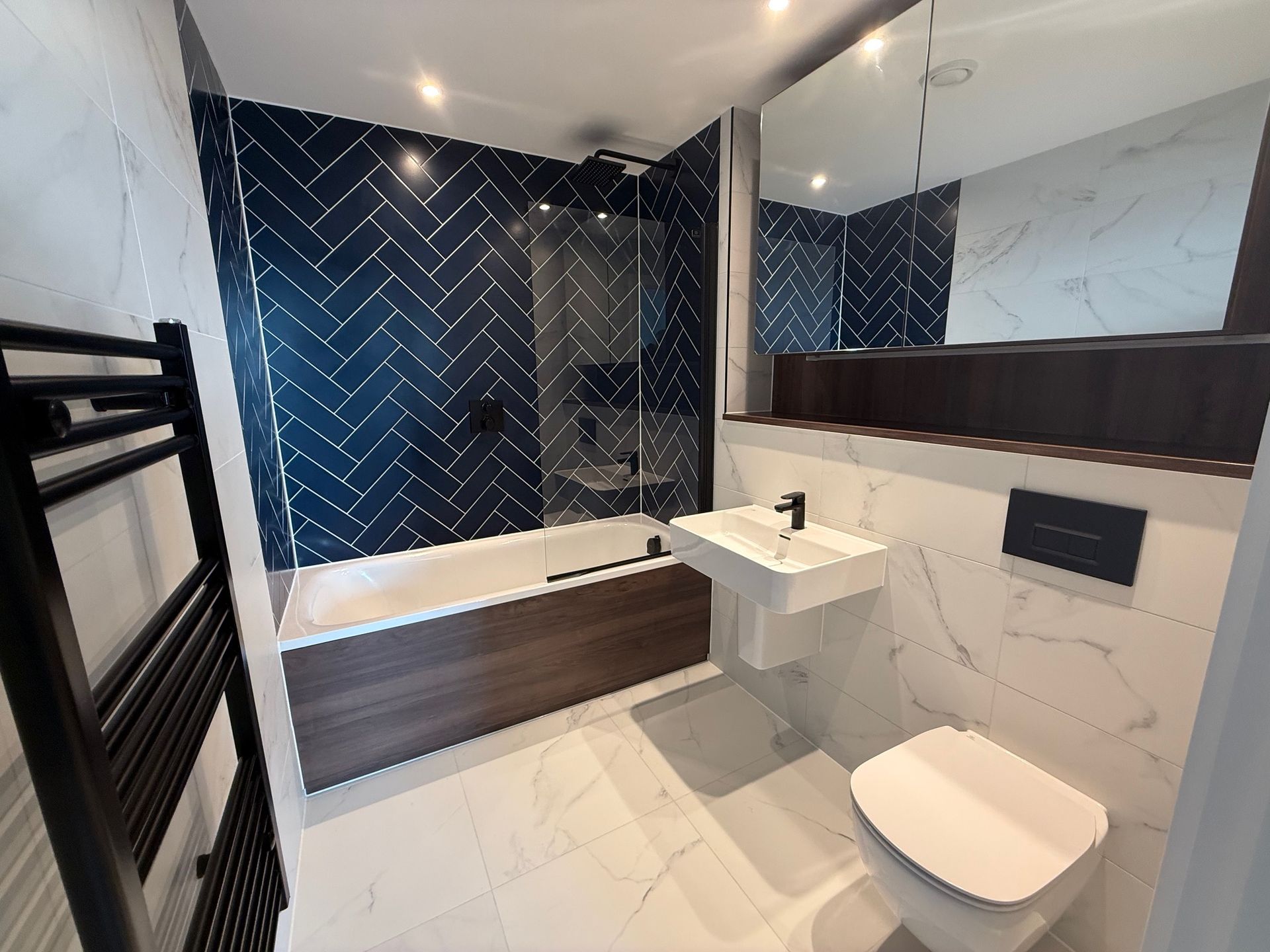 Modern bathroom with blue herringbone tile, white marble tile, dark wood accents, and black fixtures.