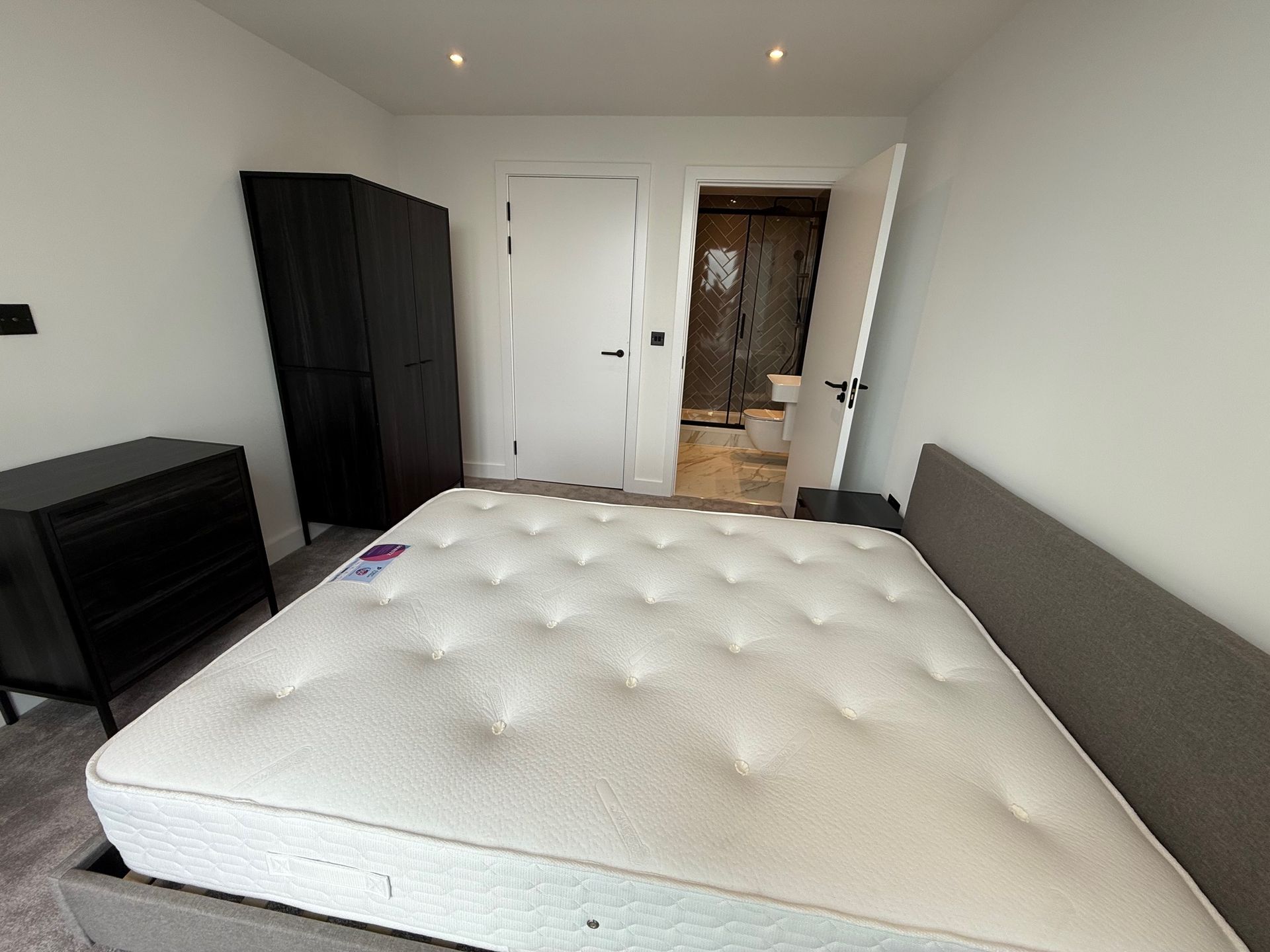 Bedroom with bed, black wardrobe, dresser, and open door to a bathroom.