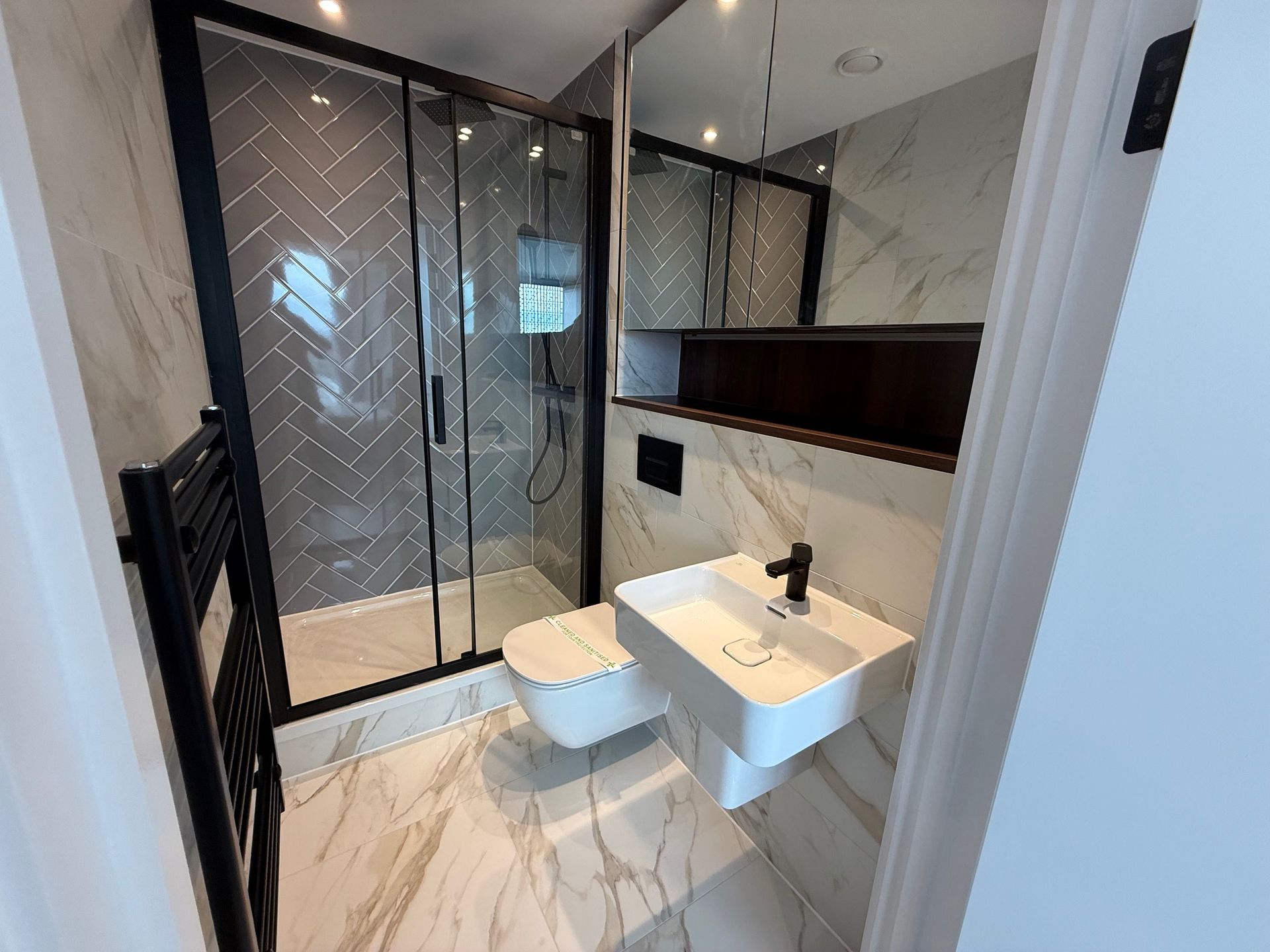 Modern bathroom with glass shower, floating sink, and white marble tiles.