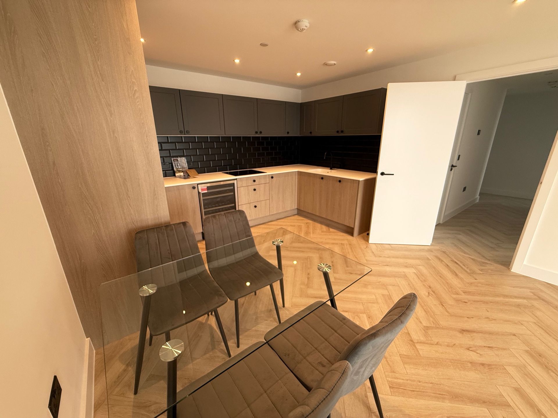 Modern kitchen with dining table and chairs, light wood floors, and dark cabinets.