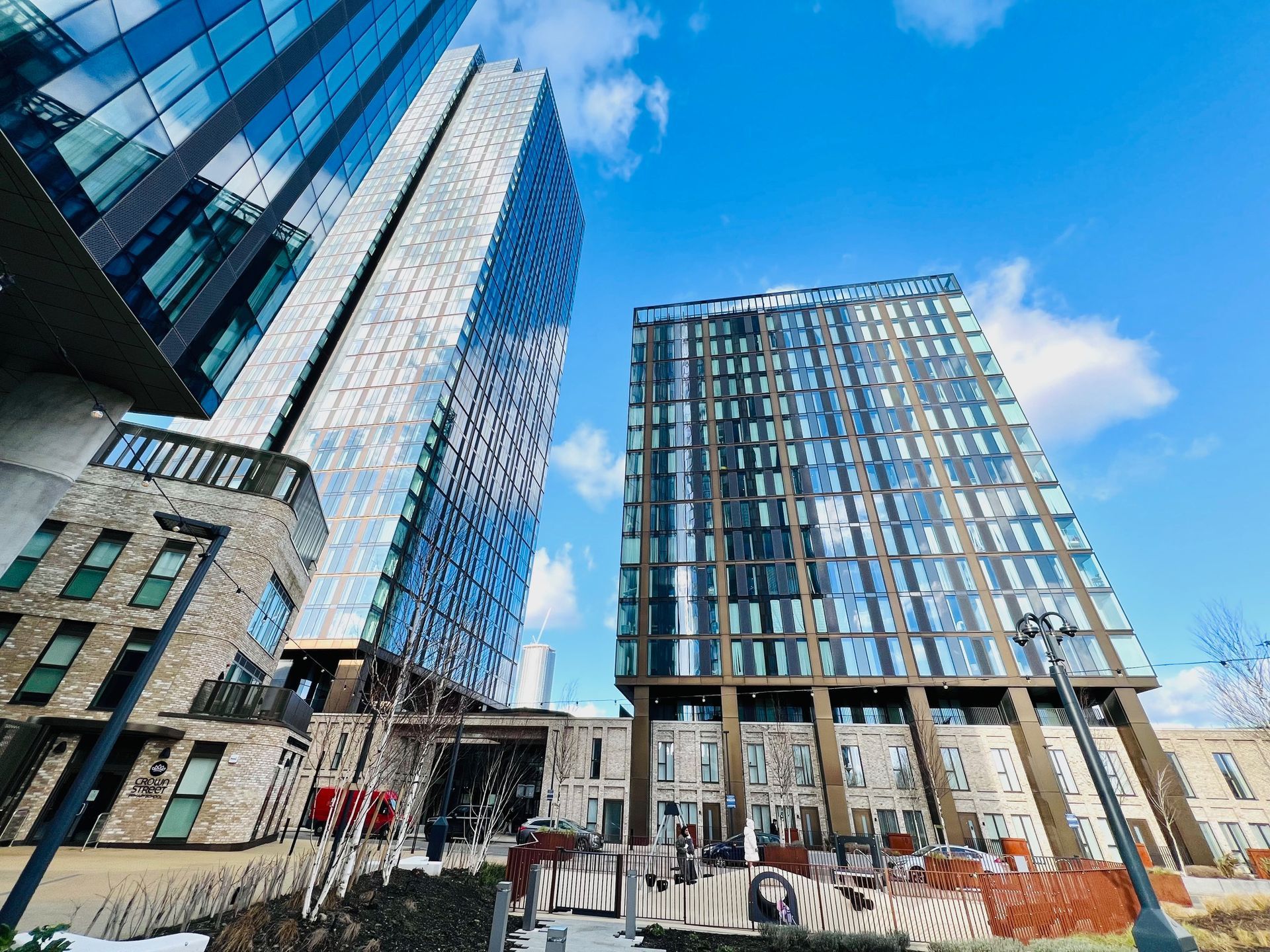 Modern high-rise buildings against a blue sky, viewed from a low angle. The architecture uses glass and brick.