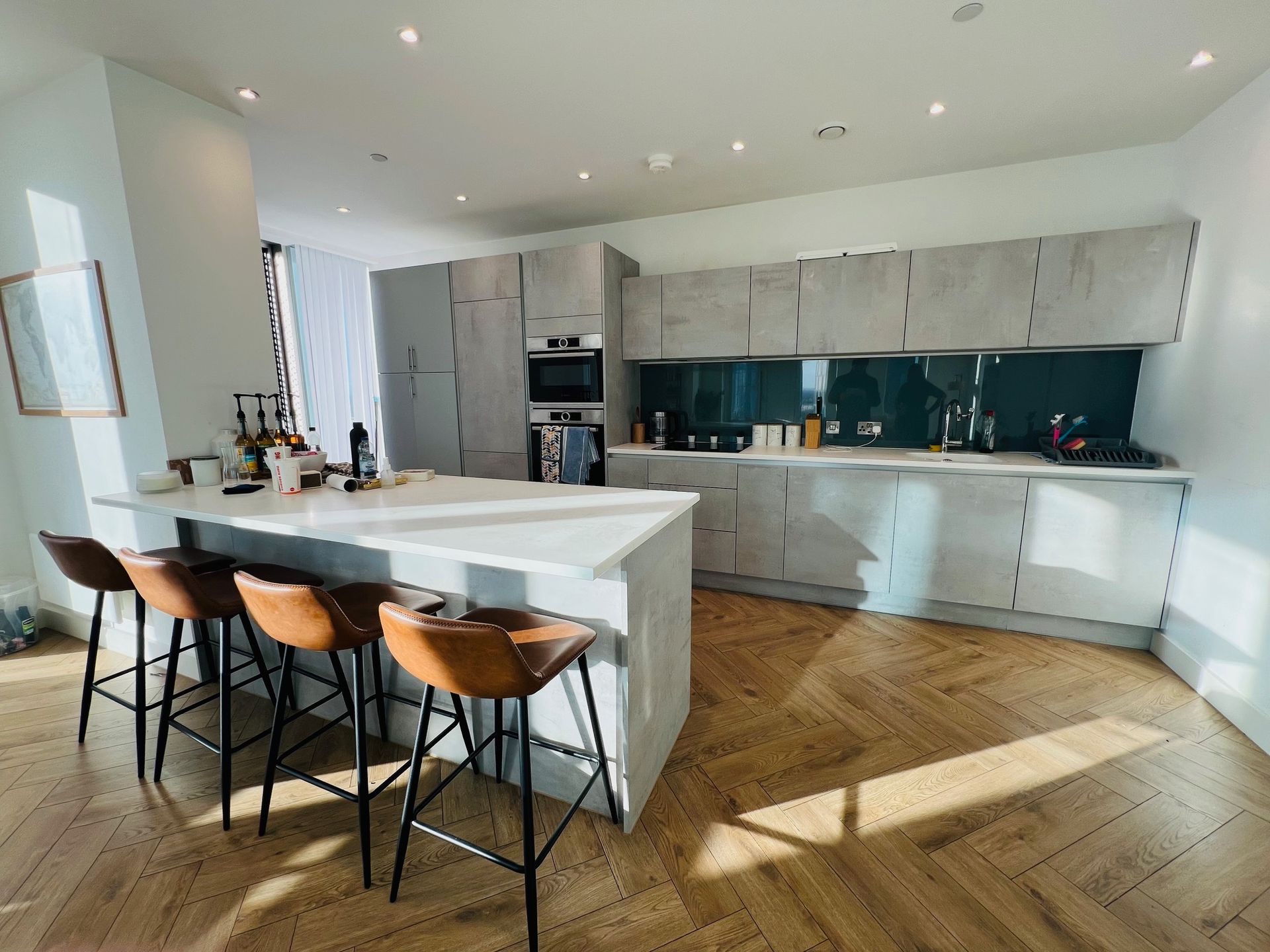 Modern kitchen with light gray cabinets, white countertop island, and brown leather bar stools.