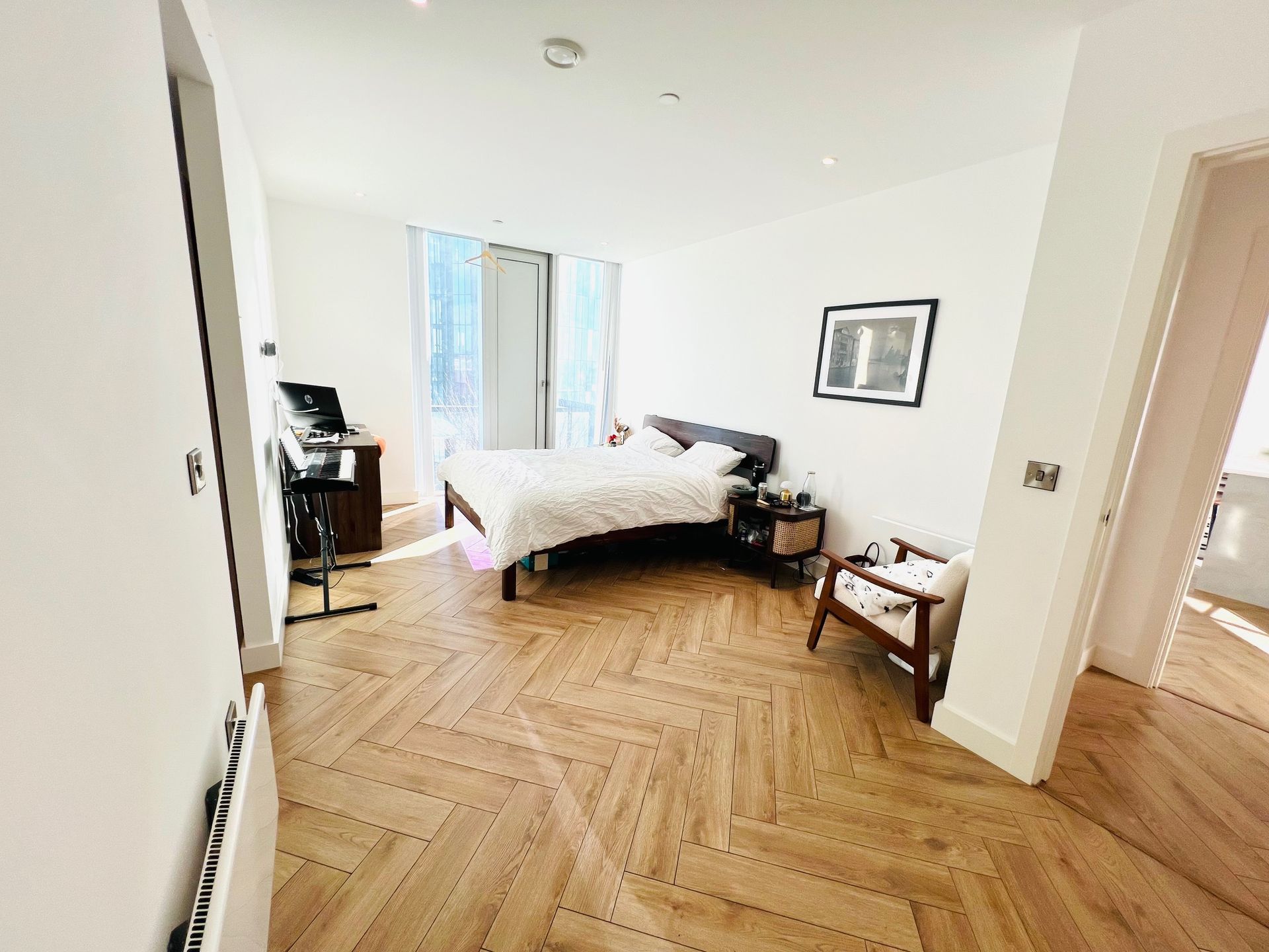 Bedroom with herringbone wood floors, bed, chair, artwork, and music stand by a window.