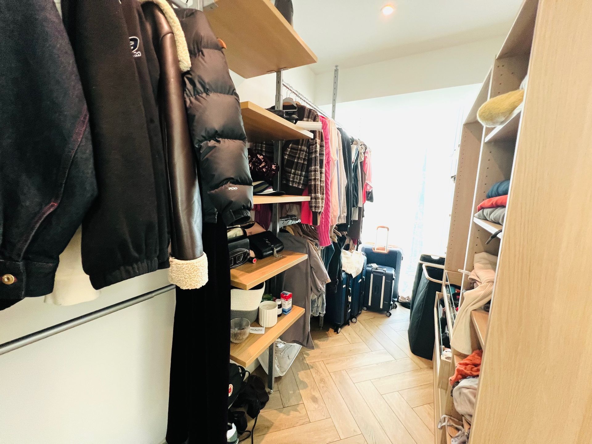 Walk-in closet with clothes on shelves and hanging. Light wood and beige tones.