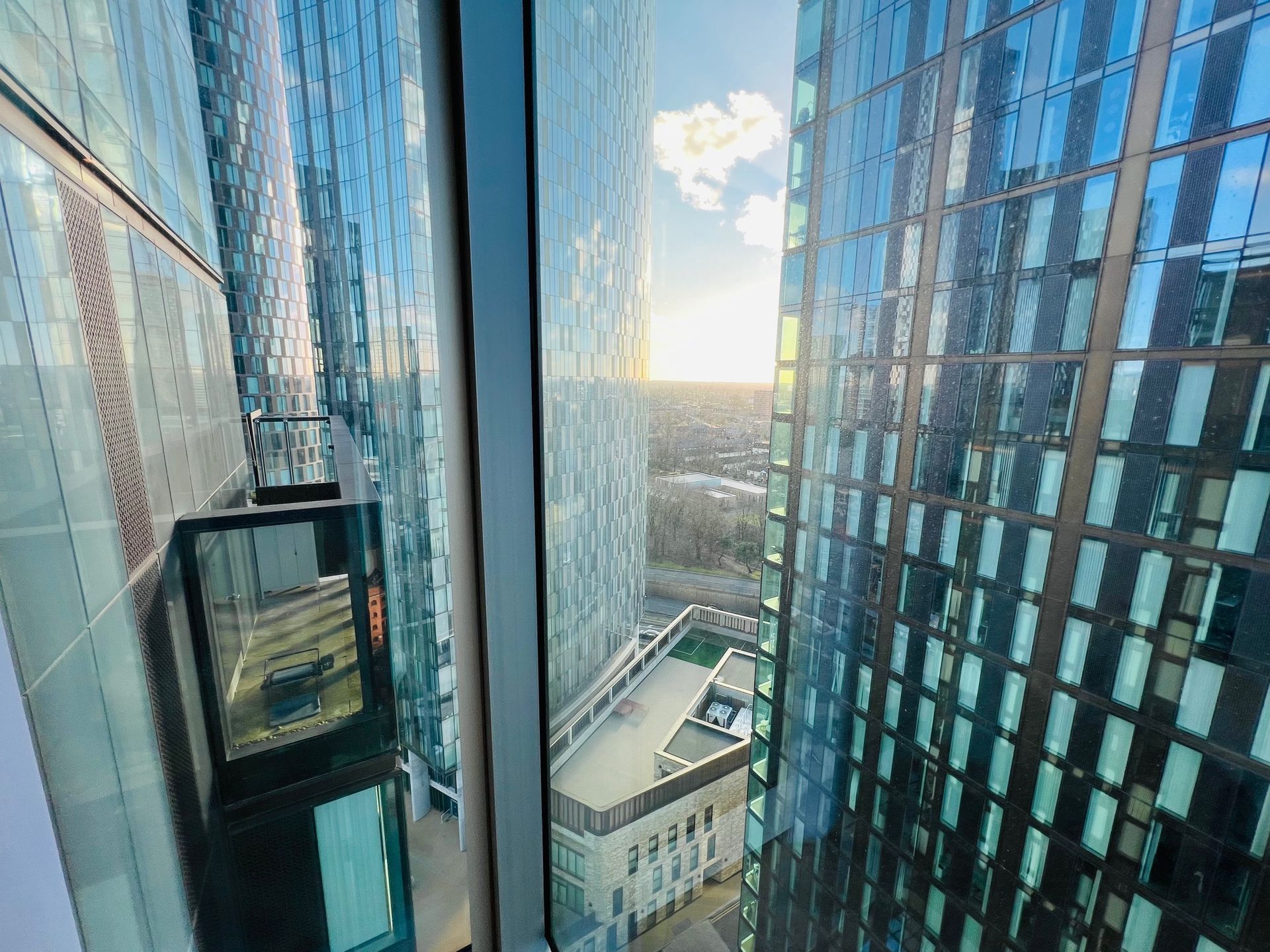 View from tall building window between other skyscrapers. Sunlight, urban setting.