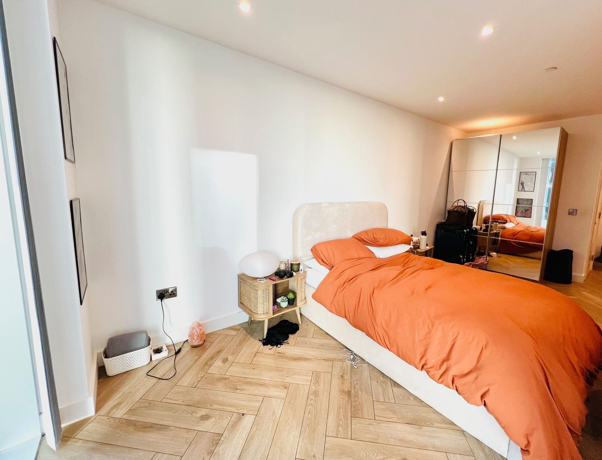Bedroom with orange bedding, light wood floors, and a large mirrored closet door.