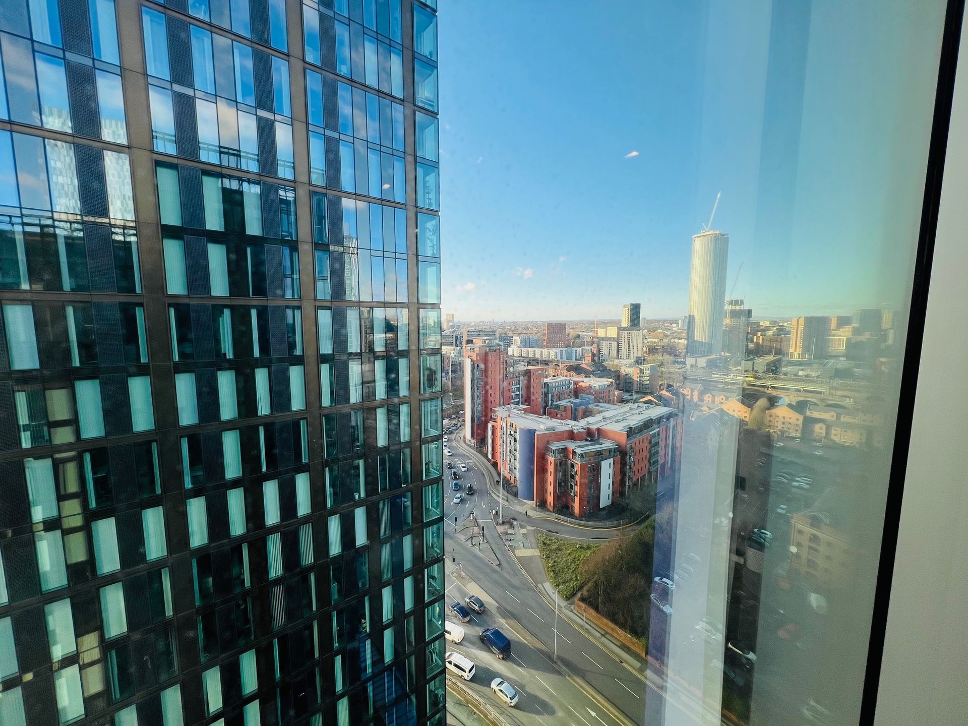 City view from a tall building, showcasing glass skyscrapers, roads, and buildings under a blue sky.