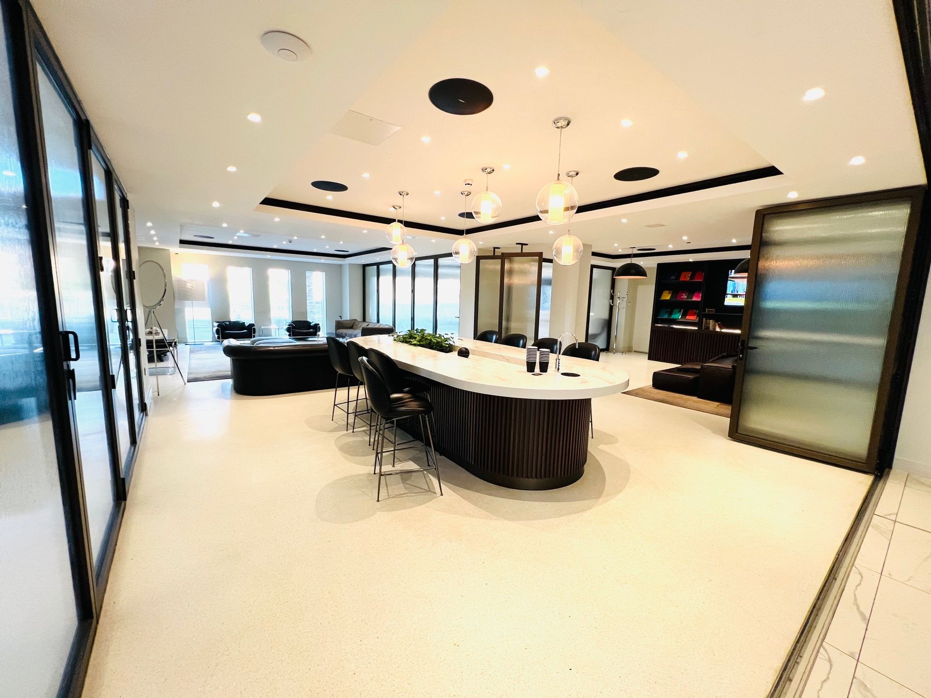 Modern interior with a long oval table, bar stools, and glass sliding doors. White and black accents throughout.