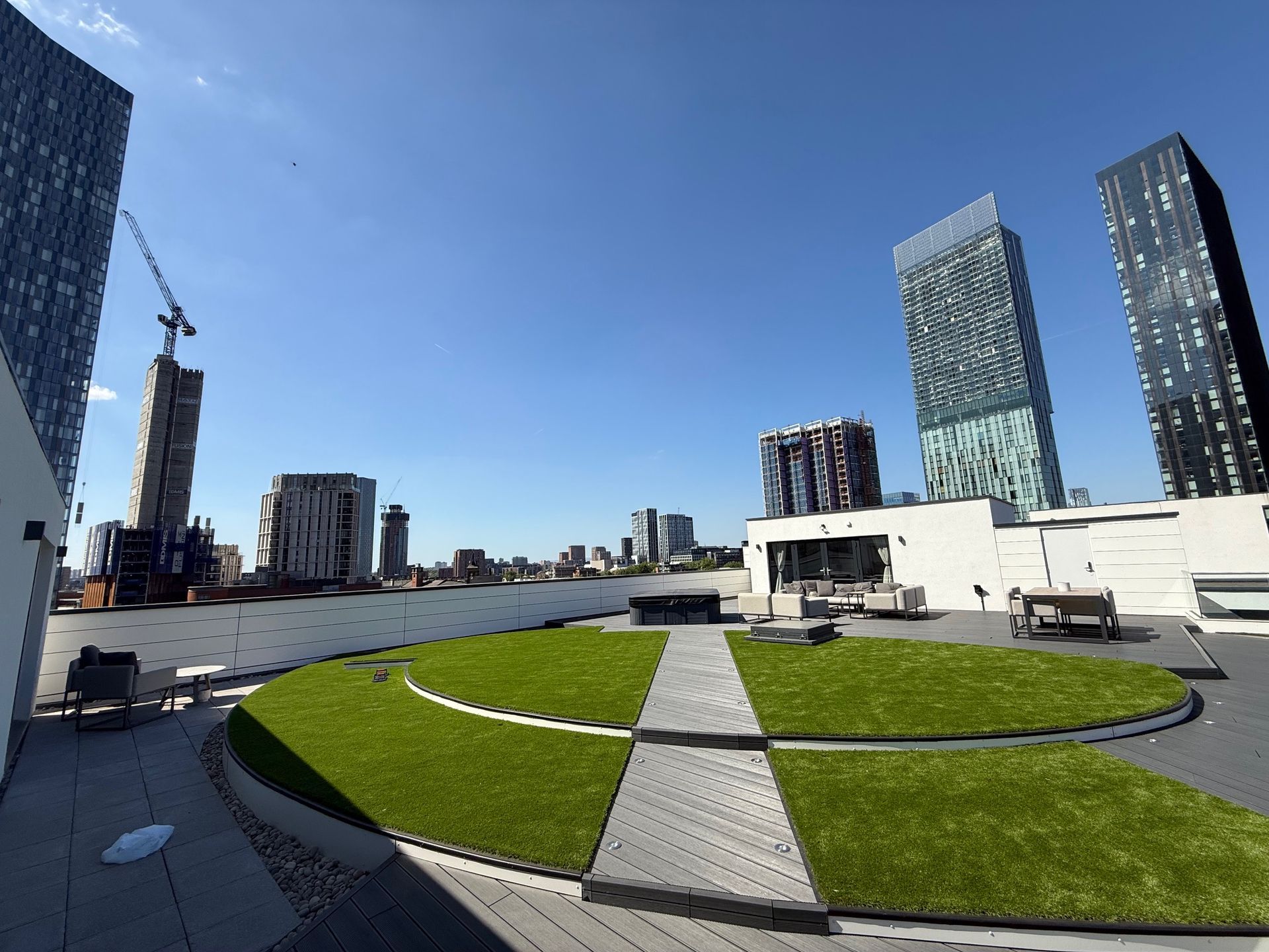 Rooftop view of a city with green spaces, modern skyscrapers under a blue sky.
