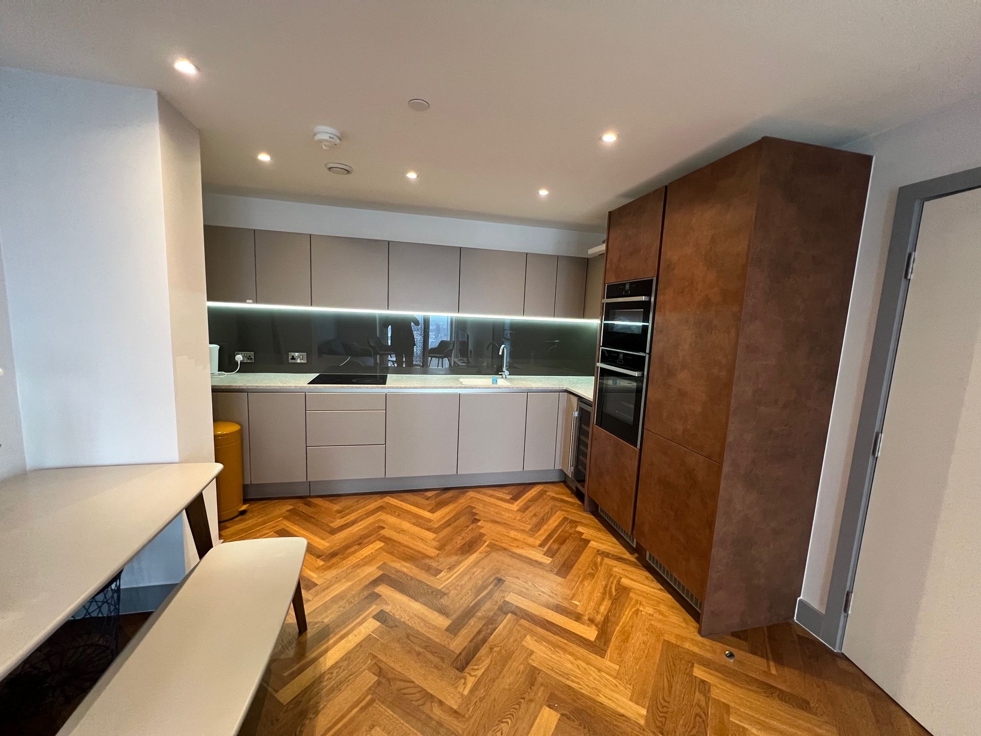 Modern kitchen with wood floor and cabinetry, featuring a table with bench seating.