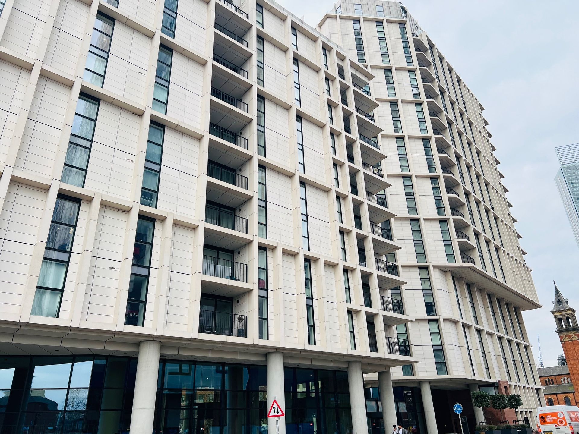 Modern apartment building with balconies, off-white facade, and glass storefront. Located in urban setting.