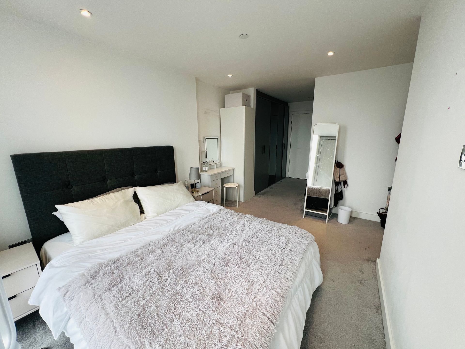 Bedroom with bed, white walls, dresser, full-length mirror, and gray carpet.
